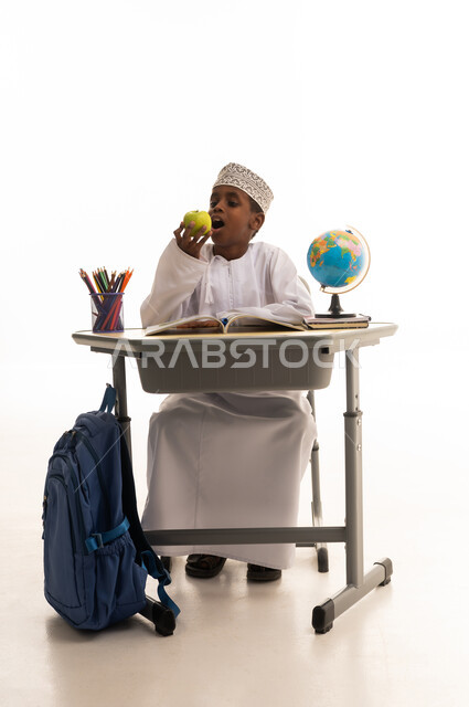 طالب مدرسي عماني يأكل تفاحة على مقعد الدراسة