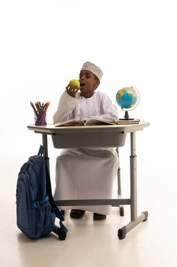 طالب مدرسي عماني يأكل تفاحة على مقعد الدراسة