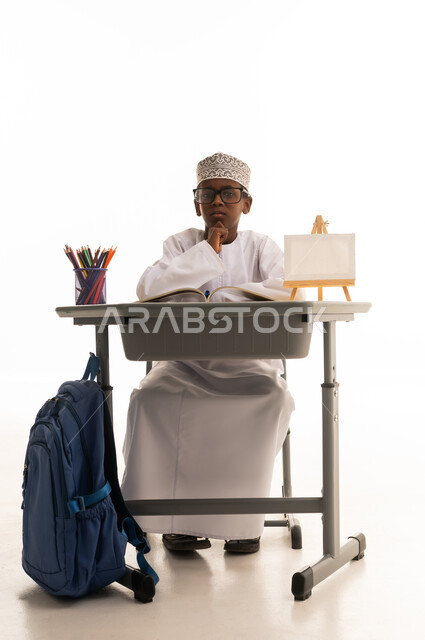 طفل عماني بالزي التقليدي خلف مقعد دراسي
