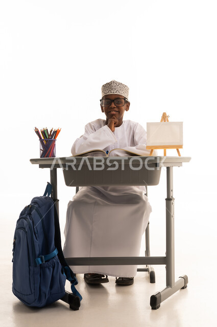 طالب عماني بالزي التقليدي يجلس خلف مقعد دراسي