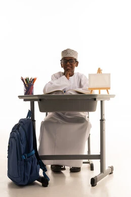 طالب عماني بالزي التقليدي يجلس خلف مقعد دراسي