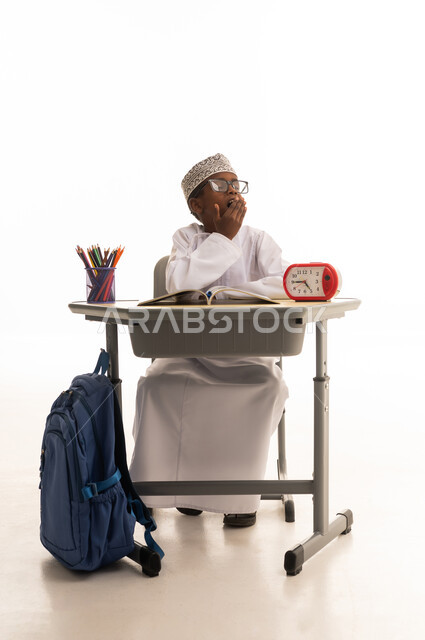 Omani Schoolboy Yawning at Desk on White Background