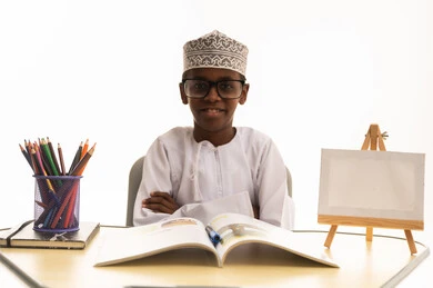 طفل عماني بالزي التقليدي يدرس على مكتب مدرسي