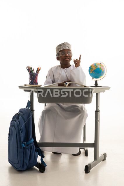 طالب عماني يجلس على مكتب دراسي ويشير للأعلى