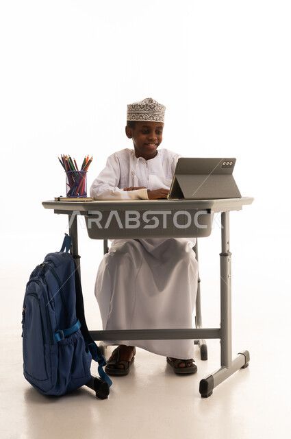 طالب عماني يستخدم جهازاً لوحياً على مكتب دراسي