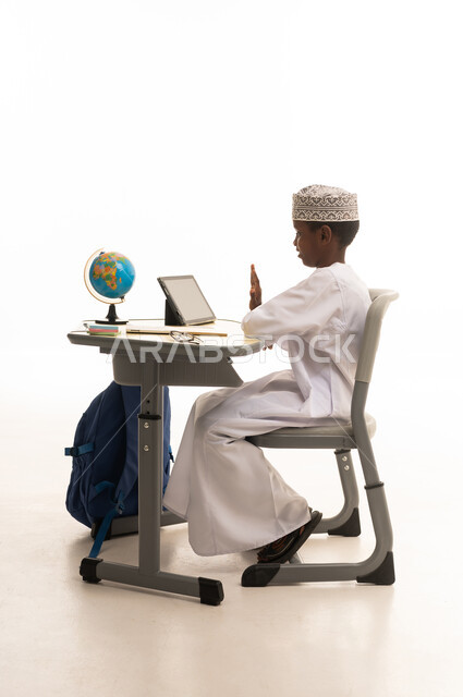 طالب عُماني يجلس خلف مكتب دراسي يستخدم جهازاً لوحياً