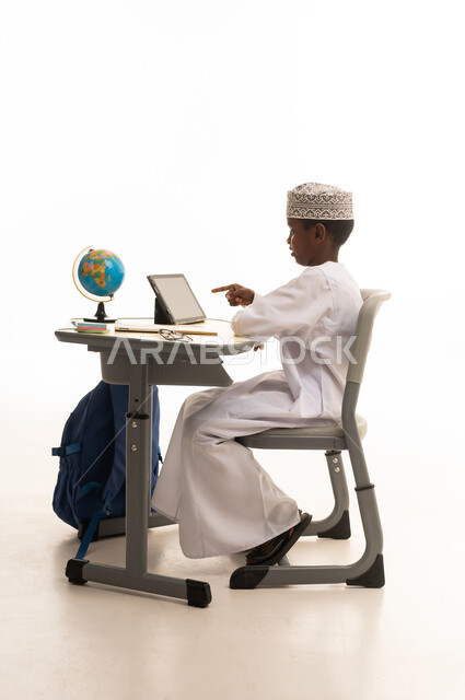 طالب عماني يستخدم جهاز لوحي على مكتب دراسي