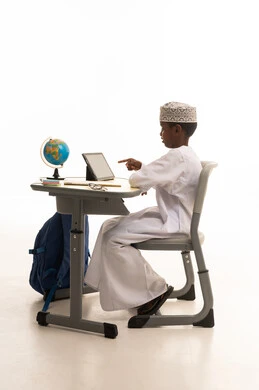 طالب عماني يستخدم جهاز لوحي على مكتب دراسي طالب عماني يستخدم جهاز لوحي على مكتب دراسي