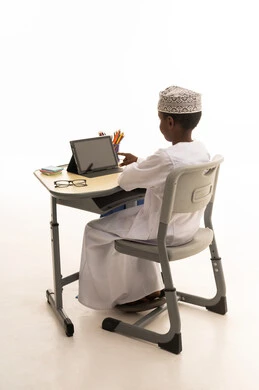 طفل عُماني يستخدم جهازاً لوحياً على مكتب مدرسي