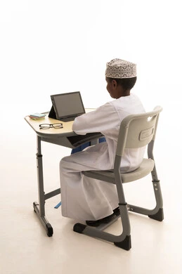 طالب عماني بالزي التقليدي يستخدم جهازاً لوحياً للدراسة