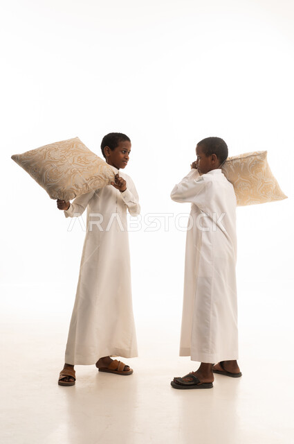 طفلان سعوديان يلعبان بالوسائد بالثياب التقليدية البيضاء
