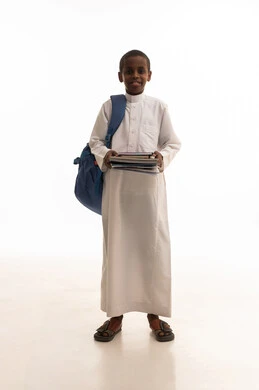 طالب سعودي بالثوب التقليدي يحمل حقيبة وكتب مدرسية