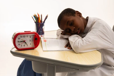 طالب متعب ينام على المكتب مع منبه أحمر