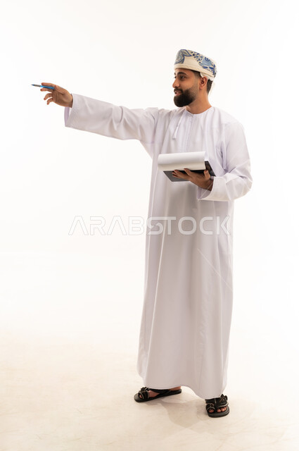 رجل عماني بالزي التقليدي يشير بيده مع دفتر