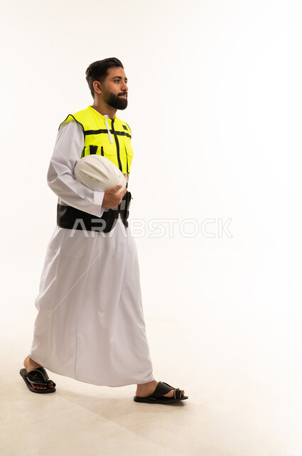 مهندس سعودي بالثوب وسترة السلامة يمشي بخلفية بيضاء