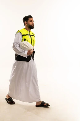 مهندس سعودي بالثوب وسترة السلامة يمشي بخلفية بيضاء
