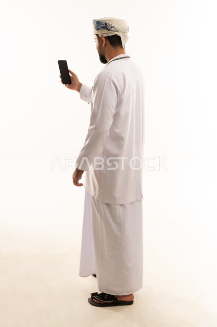 Omani Man in Traditional Dishdasha Using Smartphone