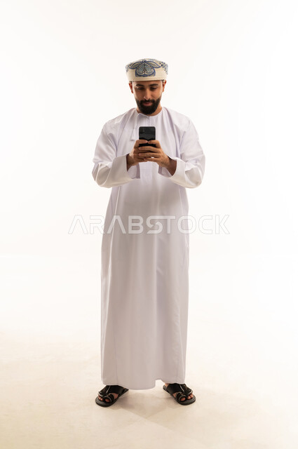 رجل عماني بالزي التقليدي يستخدم الهاتف الذكي في استوديو