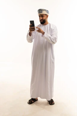 رجل عماني بالزي التقليدي يستخدم الهاتف الذكي