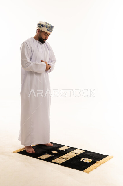 Omani Man in Traditional Dishdasha Praying on Rug