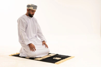 رجل عُماني يصلي على سجادة صلاة خلفية بيضاء