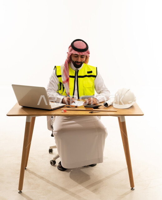 مهندس سعودي يعمل على مكتبه مع لابتوب وخوذة
