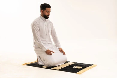 رجل عربي يصلي على السجادة بالثوب الأبيض في الاستوديو