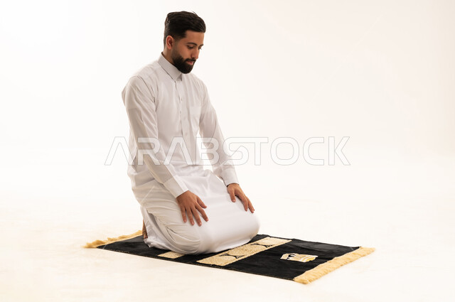 رجل سعودي يصلي على سجادة صلاة بخلفية بيضاء