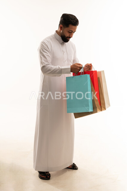 رجل سعودي يحمل حقائب تسوق ملونة بخلفية بيضاء