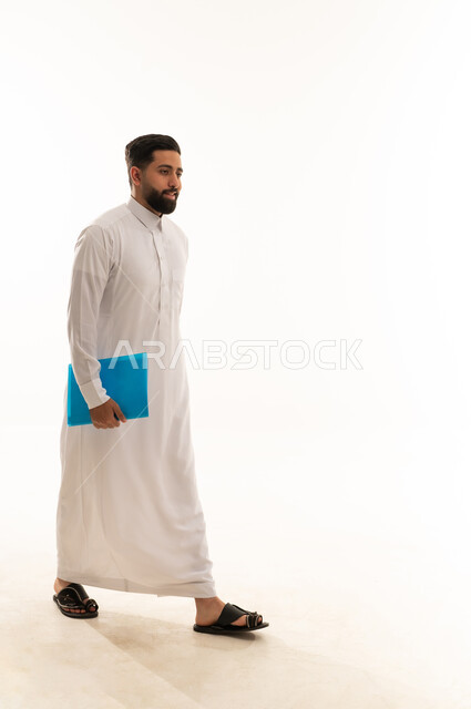 رجل سعودي بالثوب الأبيض يمشي حاملاً ملفاً