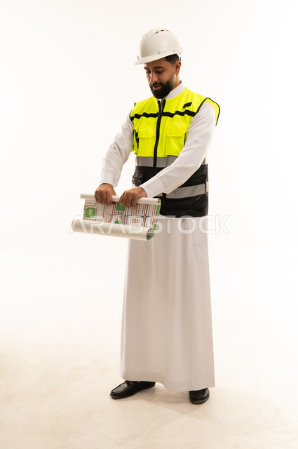 مهندس سعودي يراجع مخططات هندسية بخلفية بيضاء