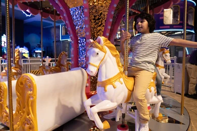 Arab Boy Riding Carousel Horse in Indoor Theme Park
