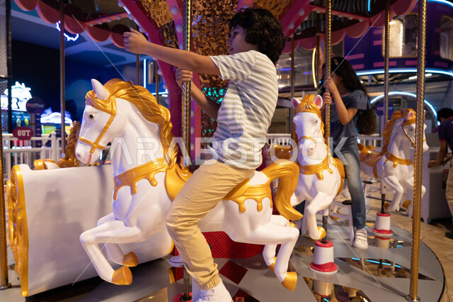 أطفال عرب يركبون لعبة الأحصنة في مدينة ملاهي مغلقة