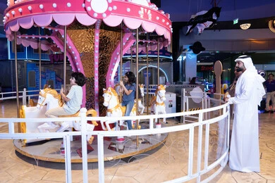 Emirati Father Watching Children on Carousel Indoor