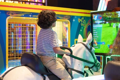 طفل يلعب بجهاز محاكاة ركوب الخيل في صالة ألعاب