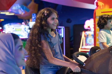 فتاة عربية تلعب في محاكي سباق داخل مدينة ملاهي