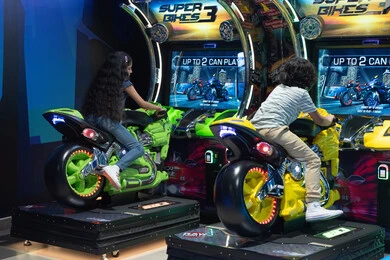 أطفال يلعبون أجهزة محاكاة الدراجات النارية في الملاهي