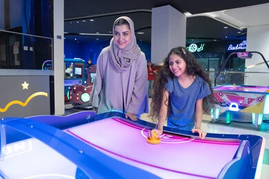 أم سعودية وابنتها تلعبان هوكي الهواء في مدينة الملاهي