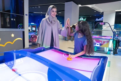 أم سعودية وابنتها تلعبان الهوكي الهوائي في صالة الألعاب