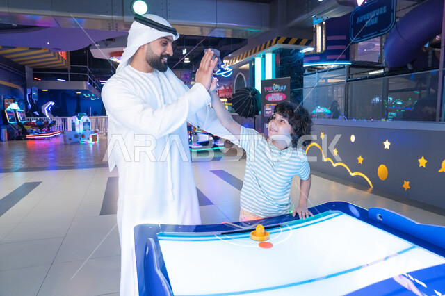 رجل إماراتي وطفل يلعبان الهوكي الهوائي في الملاهي