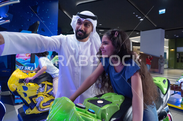 أب عربي وابنته يلعبان سباق الدراجات في الملاهي