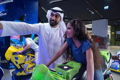 أب عربي وابنته يلعبان سباق الدراجات في الملاهي