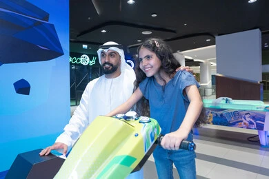 رجل إماراتي وفتاة يلعبان في صالة ألعاب ترفيهية