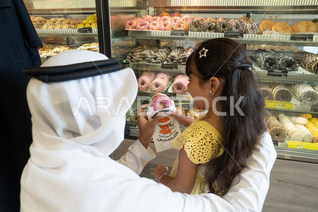 رجل إماراتي يقدم دونات لطفلة في مخبز