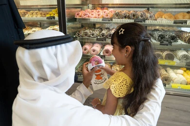 رجل إماراتي يقدم دونات لطفلة في مخبز