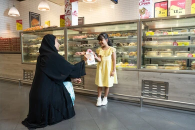 Emirati Woman Giving Pastry to Child in Bakery