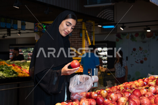 امرأة إماراتية تختار التفاح الأحمر في السوبر ماركت
