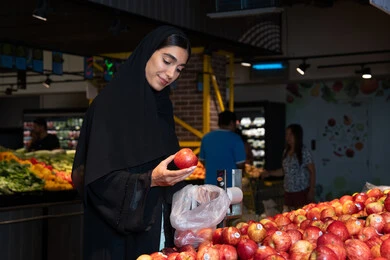 Emirati Woman Selecting Red Apples in Supermarket