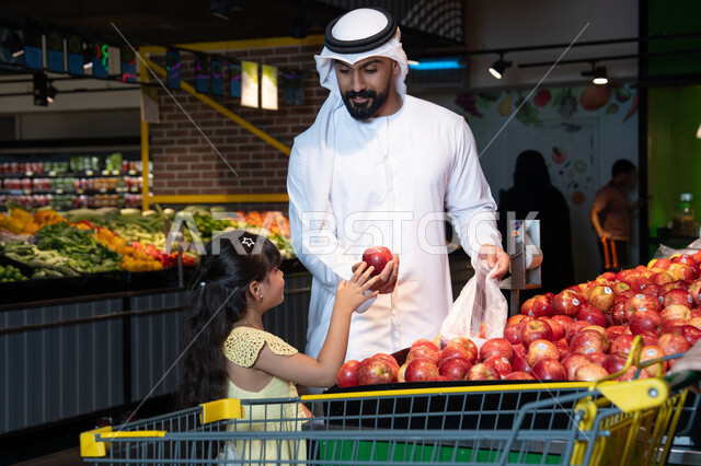رجل إماراتي وطفلة يتسوقان التفاح الطازج في السوبر ماركت