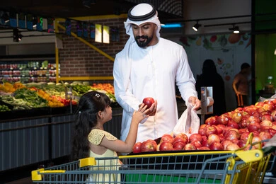 رجل إماراتي وطفلة يتسوقان التفاح الطازج في السوبر ماركت